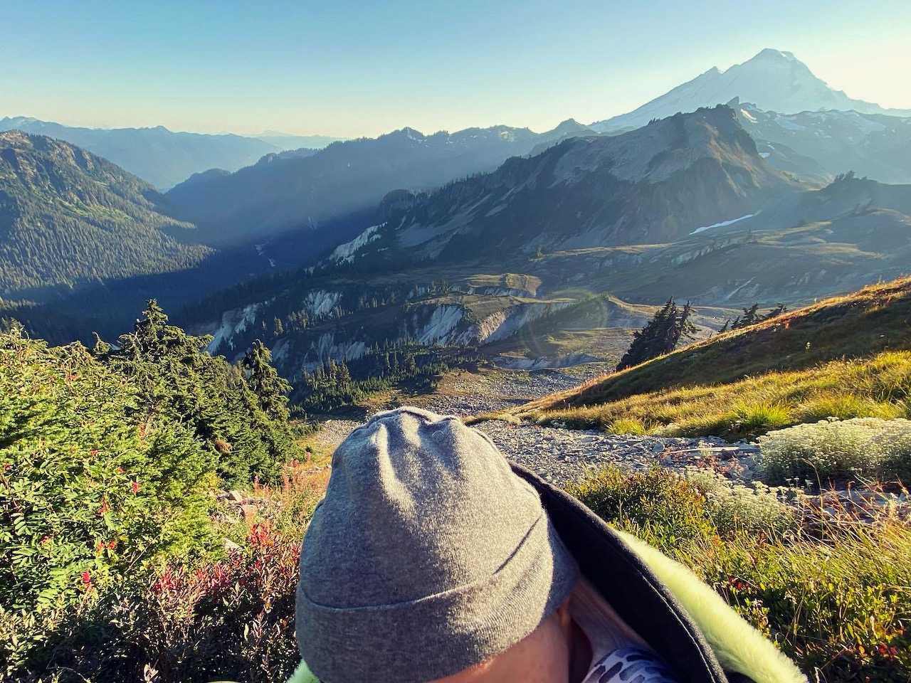 The top of a baby's head covered in a little gray hat, in the mountains